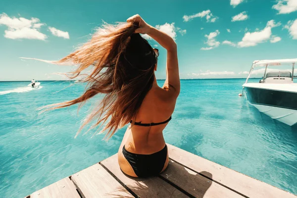 美丽的形状黑发在泳衣与太阳镜坐在码头上 享受阳光明媚的天气和海洋 向后翻转 — 图库照片