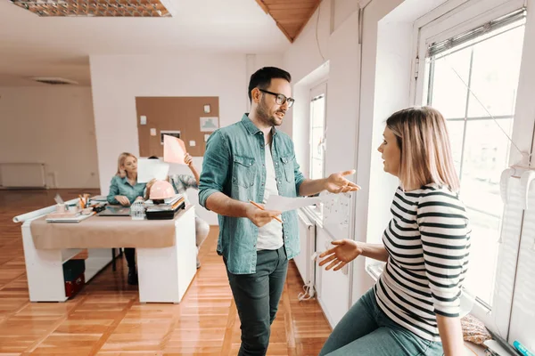 couple of designers talking near the window while their coworkers working at the office desk