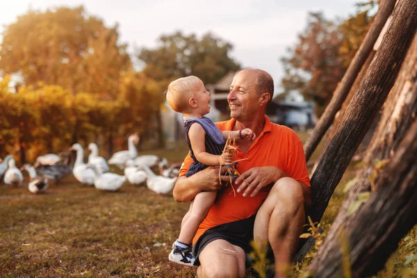 Avô Segurando Neto Sentado Chão Outono Patos Fundo — Fotografia de Stock