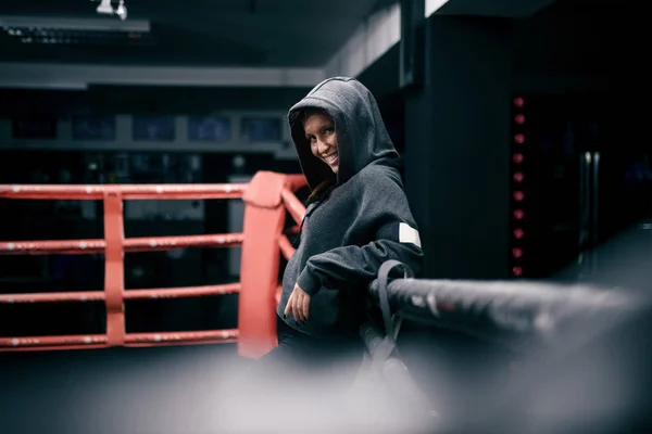 Powerful caucasian female boxer posing in ring with hoodie on head.