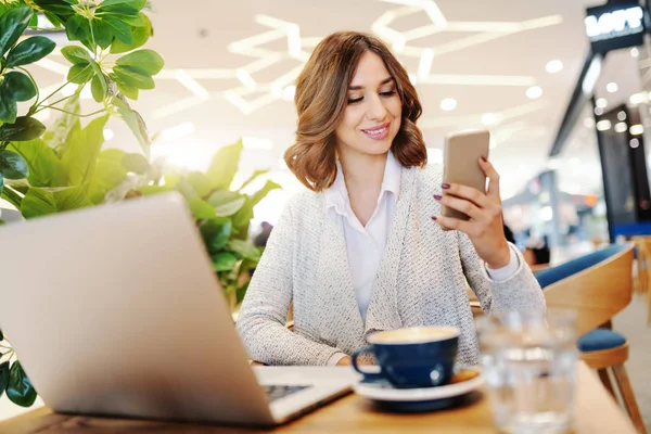 Gülümseyen Kadını Kafeteryada Otururken Akıllı Telefon Kullanarak Rahat Giyinmiş Danışma — Stok fotoğraf