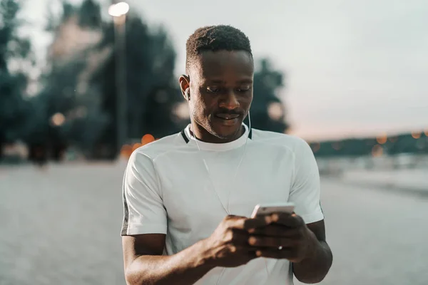 Gülümseyen Afrika Adam Uygun Kulaklarında Kulaklık Koymak Akıllı Telefon Tutarak — Stok fotoğraf