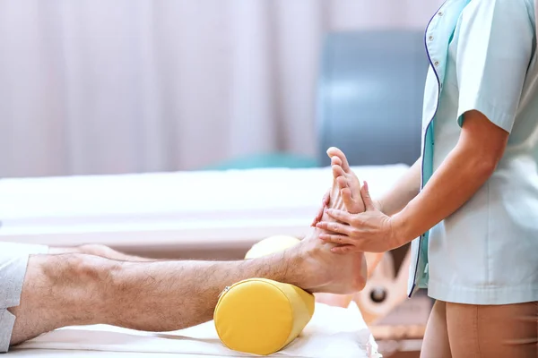 女性の看護師が男性患者の足をマッサージのクローズ アップ 整形外科医のオフィスのインテリア — ストック写真