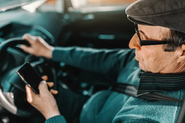 严重的白种人 头上戴着帽子 戴着眼镜 手放在方向盘上 用智能手机坐在车里 打开的窗口 — 图库照片