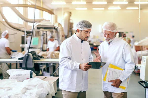 Due Operai Uniformi Bianche Sterili Piedi Fabbrica Alimentare Guardando Tablet — Foto Stock