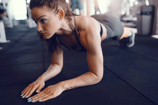 体育館の床に板をやってする若い魅力的な白人女性筋肉ボディービルダー — ストック写真