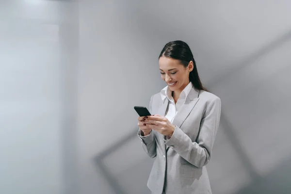 Sonriente Morena Atractiva Usando Teléfono Inteligente Ropa Formal Pie Pasillo — Foto de Stock