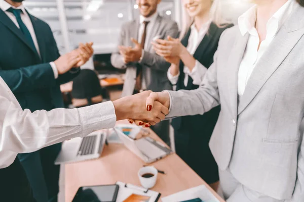 Two partners shaking hands while other colleagues clapping hands. Board room interior. Find a partner who encourages you to grow.