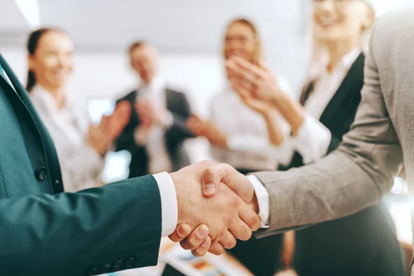 Close up of two partners shaking hands while other colleagues clapping hands. Be a boss, build an empire.