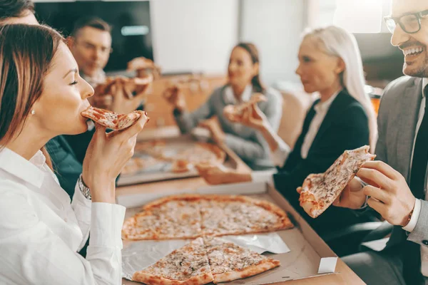 正式な服を着た幸せな同僚の小さなグループは 昼食のために一緒にピザを食べます 一緒に固執するチームを打ち負かすのは難しい — ストック写真