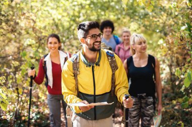 Small happy group of hikers exploring forest in the autumn. Selective focus on man leading the group and holding map. clipart