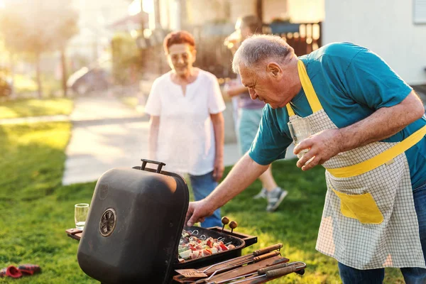 elderly happy man cooking meat at outdoor grill