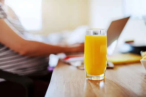 テーブルの上のガラスの新鮮なオレンジジュースのガラス バックグラウンドでは ラップトップを使用して妊娠中の女性 ジュースの選択的焦点 — ストック写真