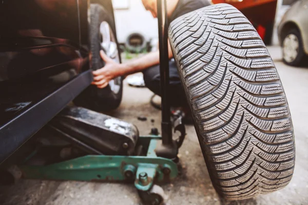 汽车修理工在车间蹲着的时候换轮胎 有选择地关注轮胎 — 图库照片