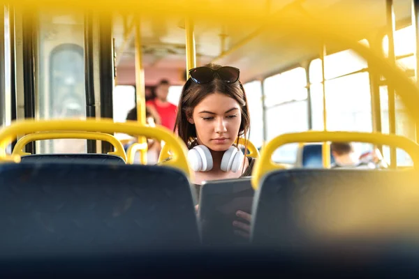 女孩带着耳机坐在公共交通中 看着平板电脑 — 图库照片
