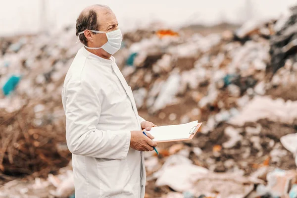 穿着白色制服的生态学家 脸上戴着剪贴板 评估损坏情况 查看垃圾填埋场 — 图库照片