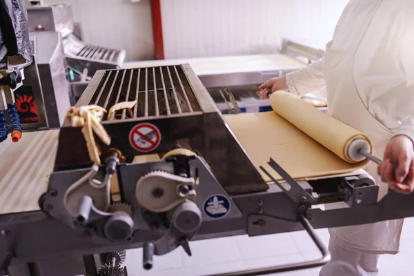 パン屋さんのマシンでパイ生地を作る白い制服で勤勉なパン屋 — ストック写真