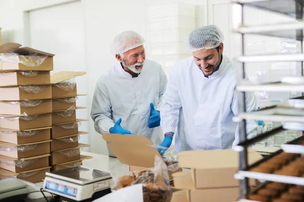 两名身穿无菌白色制服 包装饼干 站在食品厂时说话的工人 — 图库照片