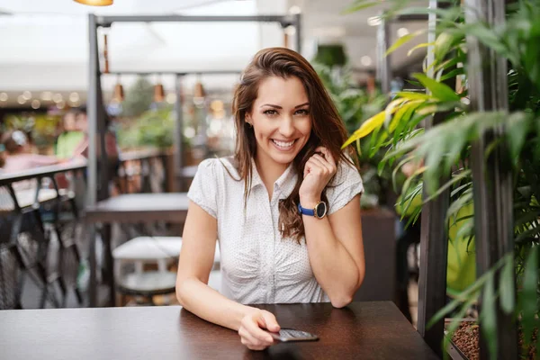Hermosa Morena Caucásica Sonriente Posando Cafetería Mientras Sostiene Teléfono Inteligente — Foto de Stock