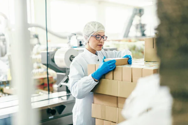 Jovem Funcionária Caixas Contagem Uniformes Estéreis Enquanto Estava Fábrica Alimentos — Fotografia de Stock
