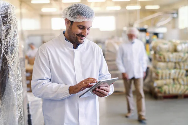 食品工場に立ちながらデータを確認するタブレットを使用して制服を着たスーパーバイザーのクローズアップ — ストック写真