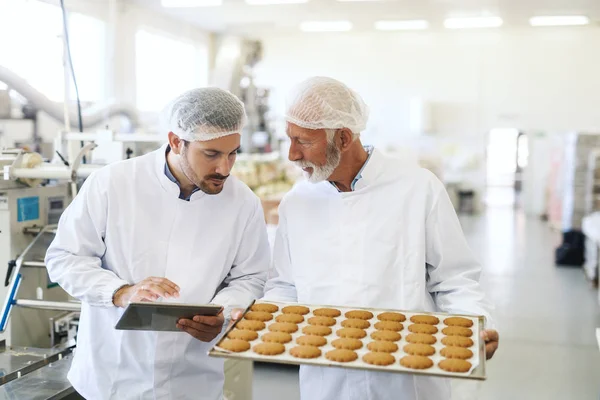 作業者は品質をチェックし タブレットを保持しながら クッキーとキャセロールを保持します 食品工場内装 — ストック写真