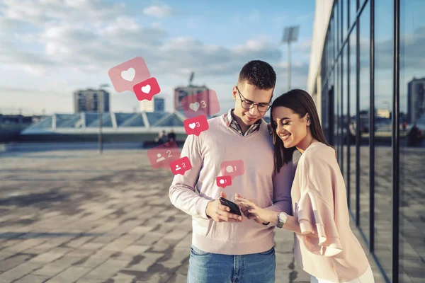 若い白人ファッショナブルなカップルがバルコニーに立って ソーシャルメディアのためにスマートフォンを使用して — ストック写真