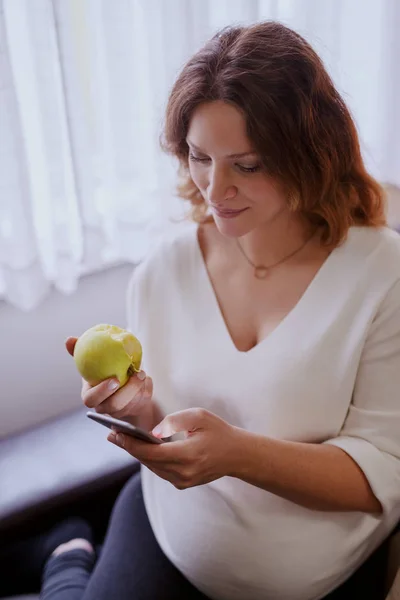 Vackra Kaukasiska Gravid Kvinna Sitter Vardagsrummet Med Hjälp Smarta Telefonen — Stockfoto