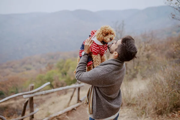 Attractive mixed race man holding his loving dog while standing in nature at fall.