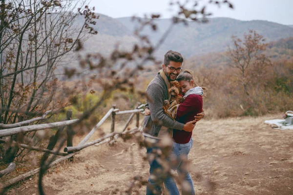 可爱的多元文化夫妇在秋天站在角上 与他们的狗拥抱他们之间 背景丘陵和森林 — 图库照片