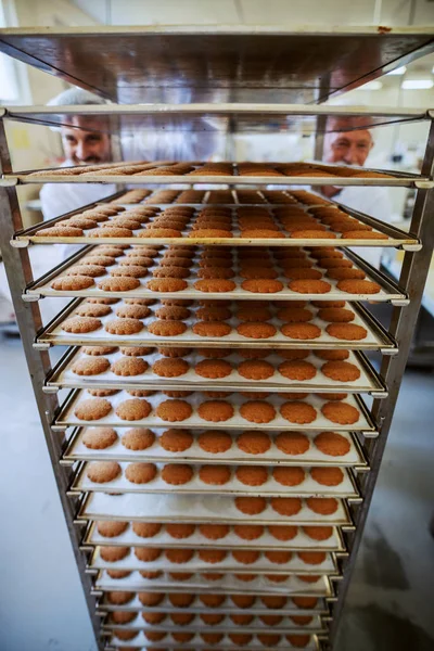 Dois Funcionários Fábrica Alimentos Empurrando Bandejas Com Biscoitos Frescos Interior — Fotografia de Stock