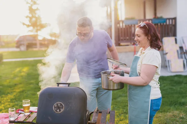 图片显示的是一对中年夫妇在自家后院做烧烤 夏日的家庭午餐 — 图库照片