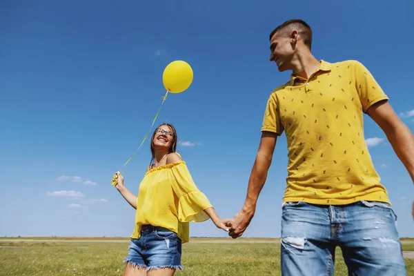 可爱的白种人夫妇身着蓝色和黄色服装手牵手 女孩拿着黄色气球 — 图库照片