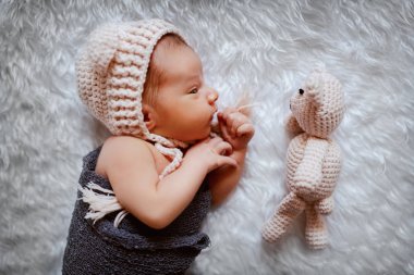 Top view of beautiful newborn baby wrapped in wool scarf and with cap on head lying next to toy. clipart