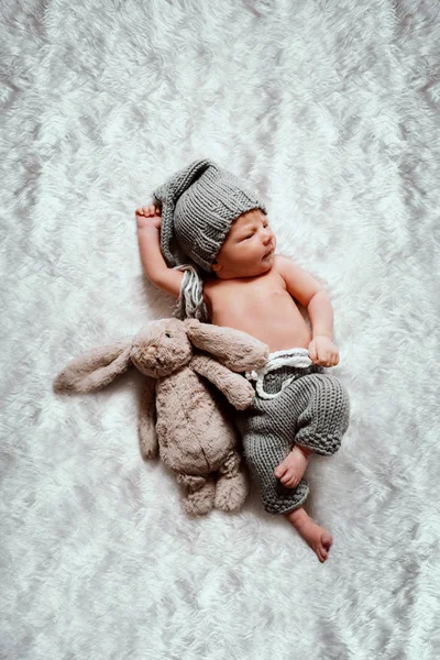 ニットパンツに身を包み ウサギのおもちゃの隣に毛布の上に横たわっている頭の上にニットキャップを持つ新生児白人の少年のトップビュー — ストック写真