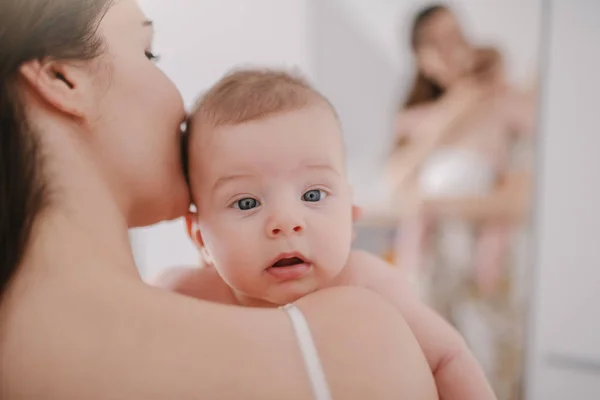 白人の母親が愛する6ヶ月の息子を抱きしめてキスするクローズアップ 混乱した表情でカメラを見ている赤ちゃん — ストック写真