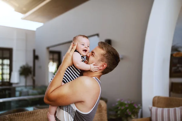 Happy handsome Caucasian father hugging his loving 6 months old son while standing indoors. Baby is laughing and hugging father.
