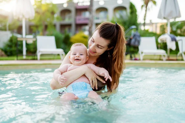 美しい白人の母親がスイミングプールに立って 彼女の6ヶ月の息子を保持しています カメラを見て 笑顔の赤ちゃん — ストック写真