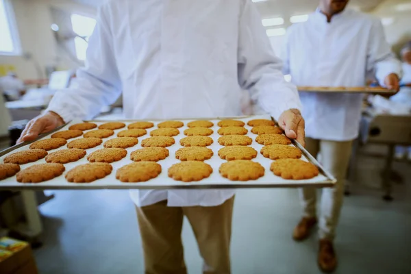 クッキー付きトレイを運ぶ無菌ユニフォームの食品工場労働者 — ストック写真