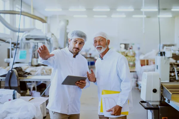 Twee Kaukasische Toezichthouders Witte Steriele Uniformen Staan Levensmiddelen Fabriek Jongere — Stockfoto