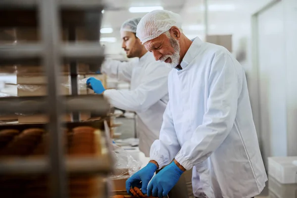 無菌のユニフォームを着た2人の勤勉な食品工場の従業員がクッキーを箱に詰め込む — ストック写真