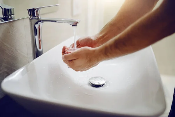 Close up male cupped hands under tap in bathroom. Morning routine.