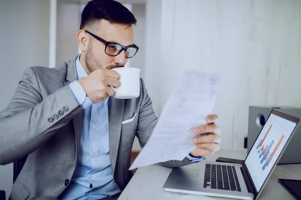 일하는 양복을 사무실에 안경으로 보고서를 커피를 마시는 집중하였다 노트북 있습니다 — 스톡 사진