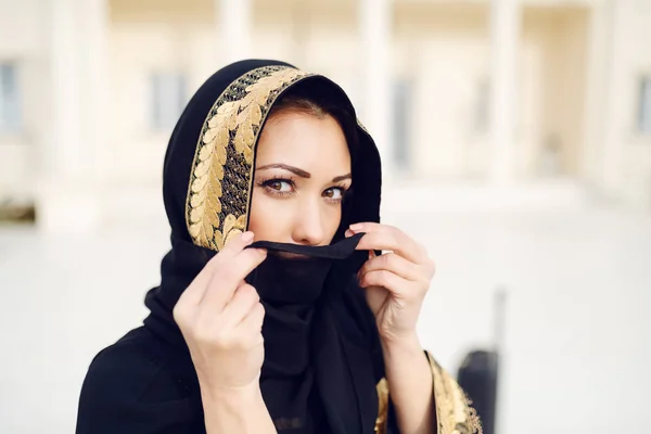 一个漂亮的穆斯林妇女站在室外 一边用围巾遮住脸 一边看着相机的画像 — 图库照片