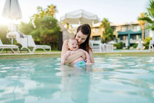 美しい白人の母親がスイミングプールに立って 彼女の6ヶ月の息子を保持しています 楽しんで微笑む赤ちゃん — ストック写真