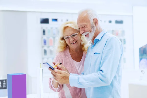 Bonito Sorrindo Casal Sênior Loja Tecnologia Experimentando Novo Telefone Inteligente — Fotografia de Stock