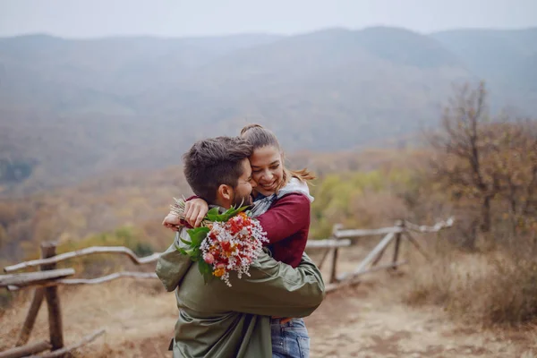 自然の中で抱き合う幸せな多文化カップル ガールフレンドを抱きしめる男と花束を持つ女性 秋の季節 — ストック写真