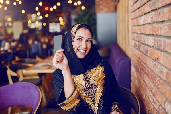 华丽的穆斯林妇女穿着传统服装的肖像要求支票和持有信用卡 而坐在咖啡馆 — 图库照片