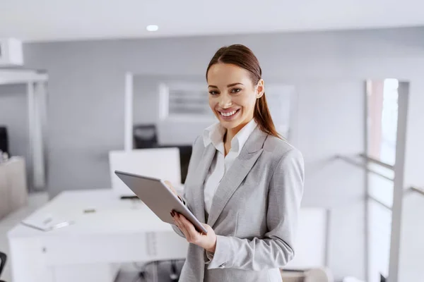 面带微笑的白种人女商人穿着正装站在办公室里 用平板电脑 — 图库照片