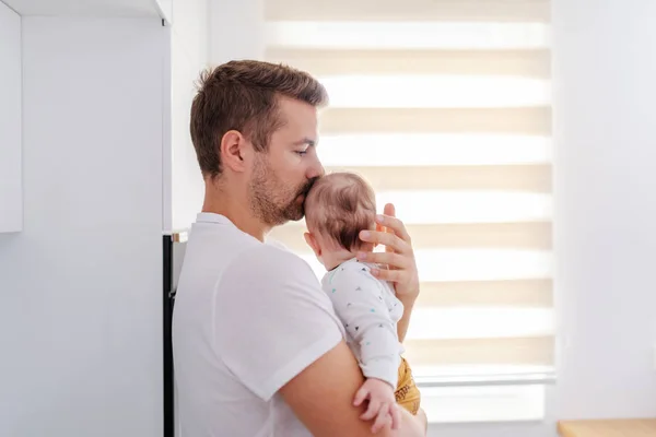 侧观关心英俊的高加索年轻爸爸抱着他可爱的6个月大的男婴站在窗边 无条件的爱情概念 — 图库照片